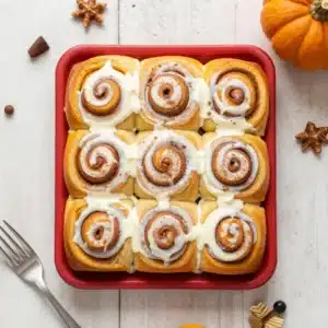 Pumpkin Cinnamon Rolls with Real Pumpkin and Spice 32 Fresh pumpkin cinnamon rolls topped with creamy icing on a serving plate